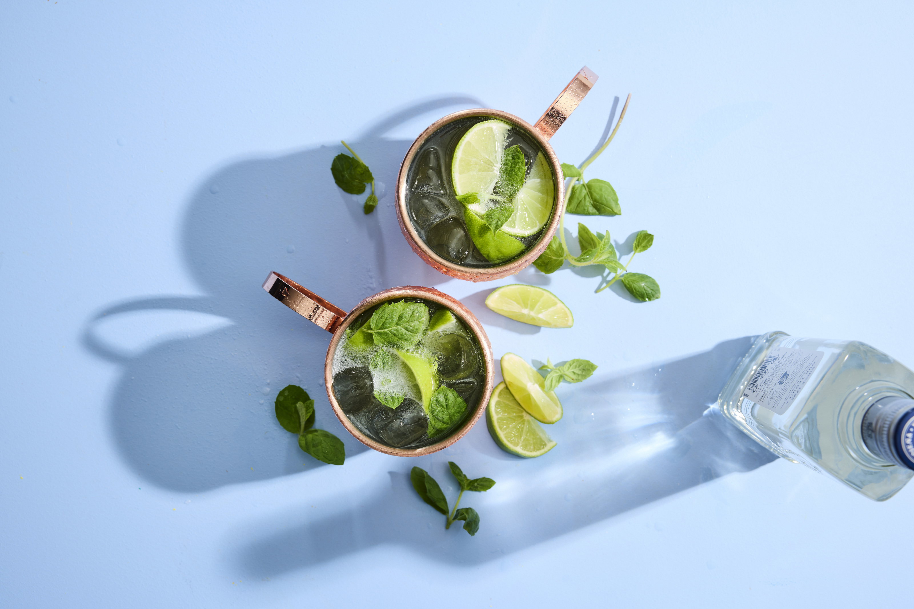 Ylhäältäpäin otettu kuva drinkkilaseista, joissa on moscow-mule drinkki vaaleansinistä taustaa vasten.